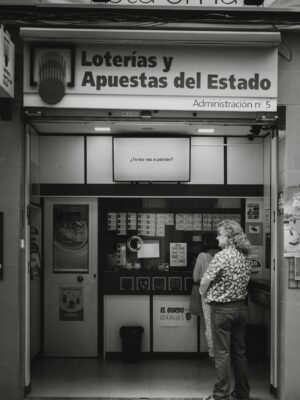 A candid black and white capture of people waiting outside a lottery kiosk.