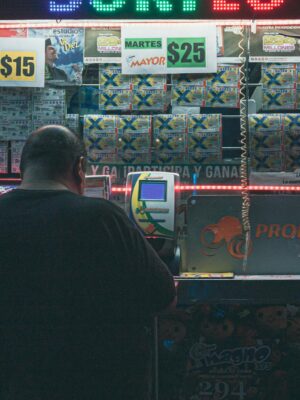 A man purchasing a lottery ticket at an illuminated kiosk in Mexico City, highlighting risk and hope.