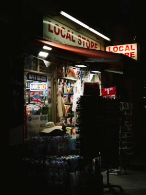Brightly lit local store front at night, showcasing a variety of goods.
